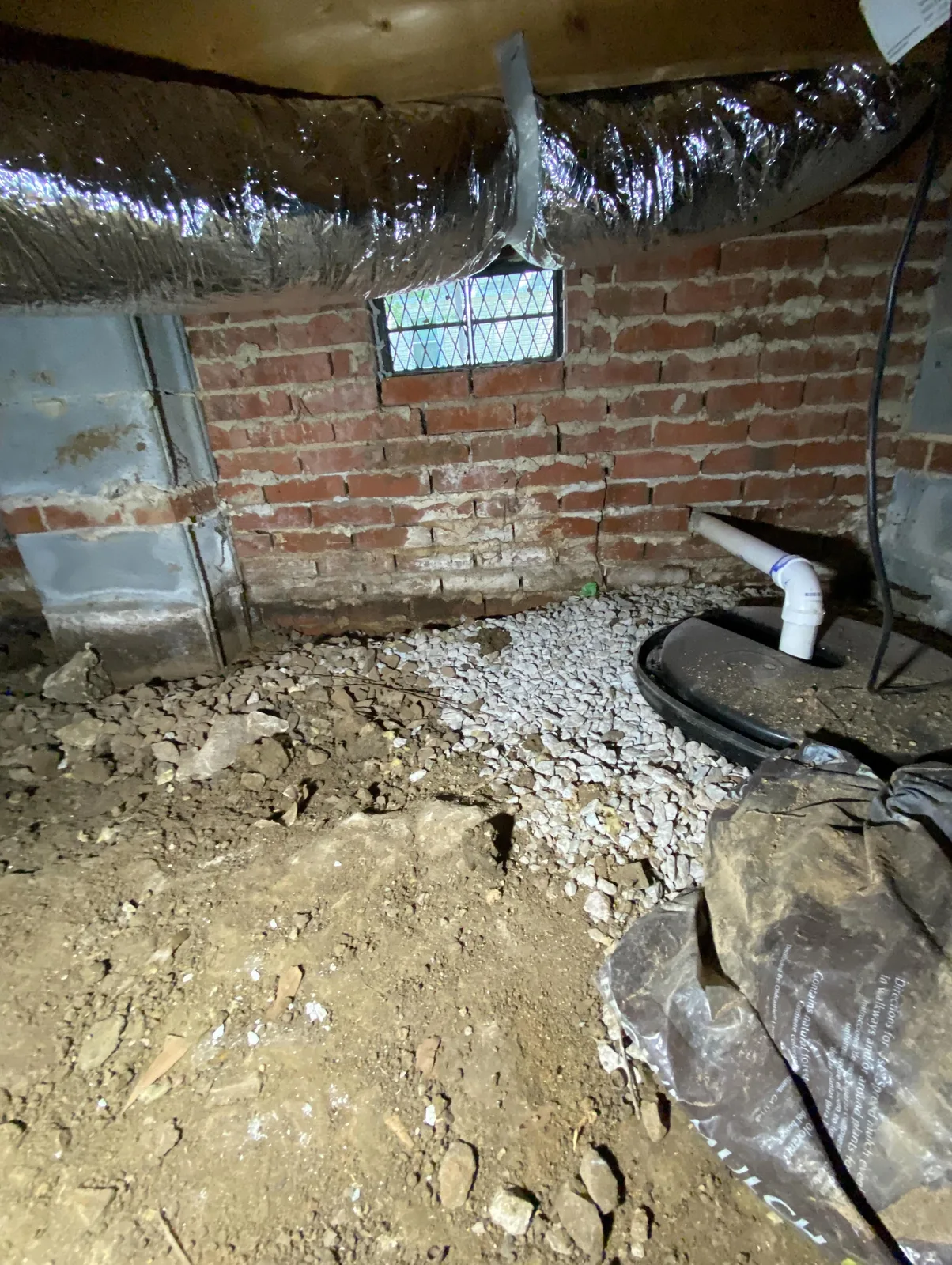 Crawlspace with bare dirt floor and exposed brick foundation wall before encapsulation